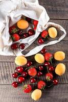 Reusable bag with apricot, strawberry and cherry on wooden table background. Zero waste concept photo