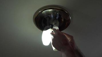 as mãos dos homens estão enroscando uma lâmpada economizadora de energia em uma pequena lâmpada no teto. video