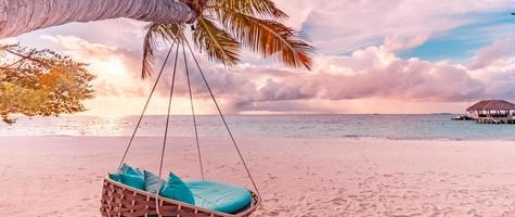 Tropical beach sunset landscape panorama beach swing or hammock and sunset sky white sand and calm sea for beach banner. Perfect beach scene vacation and summer holiday concept. Boost up color process photo