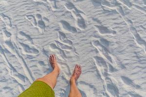 Feet on sea sand and wave, Vacation on ocean beach, Summer holiday. Man with green pants looking down on white sand photo