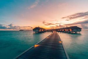 Beautiful sky and sea water, luxury tropical resort, water villas with lights under sunset. Summer island background, luxurious vacation banner. Tranquil, relaxing mood, inspirational nature landscape photo