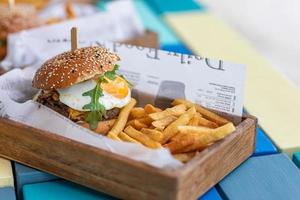 Delicious homemade burgers of beef, cheese and vegetables french fries in old wooden board at blurred outdoors restaurant background photo