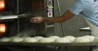 boulanger saupoudrant le levain sur la plaque de cuisson avec de la farine avant la cuisson à la cuisine de la boulangerie - ralenti video