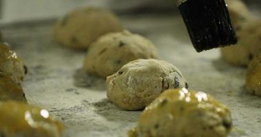 boulanger appliquant un lavage aux œufs avec un pinceau à pâtisserie sur des biscuits aux raisins secs sur un plateau avant la cuisson - ralenti video