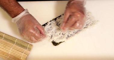 mains d'un chef de sushi étalant du riz finement sur la feuille d'une algue nori pour les rouleaux de sushi. - prise de vue en plongée video