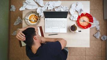 freelancer masculino trabalhando no laptop em casa na desordem e no caos. bagunça na mesa. homem trabalha remotamente entre o lixo em um apartamento de solteiro. vista do topo video