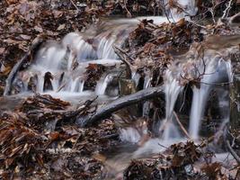 small flowing river due to snow melt forming a clean cascade with fresh cool water surrounded by vegetation mountain photo