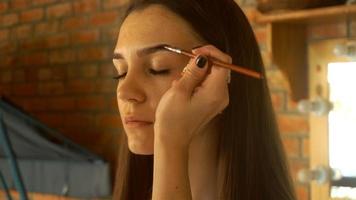 maquiador pinta as sobrancelhas de uma jovem, tinta profissional escura e pincel video