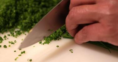 capocuoco affettare verde cipolla erba cipollina utilizzando un' acuto coltello su un' bianca chopping tavola. - vicino su tiro video