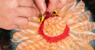 adicionando flores coloridas como decoração a um prato de delicioso sashimi de salmão com ovas - close-up video