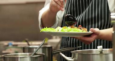 chef vertiendo salsa encima de la ensalada en un plato en la cocina de un restaurante. - tiro medio video