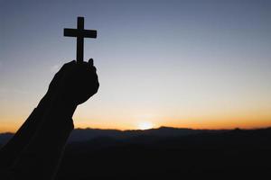 silueta de manos sosteniendo una cruz de madera en el fondo del amanecer, crucifijo, símbolo de fe. foto