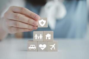 Insurance concept. Protection against a possible eventuality. Hand holding security symbol and house, car, family, travel and health care on wooden block. Life assurance concept. photo