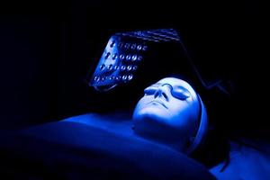 mujer joven que tiene un tratamiento de terapia facial con luz led azul en un salón de belleza.