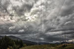High voltage towers with electricity transmission power lines in country under dark clouds