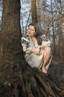 Close up woman in linen dress with embroidery sitting near tree portrait picture photo