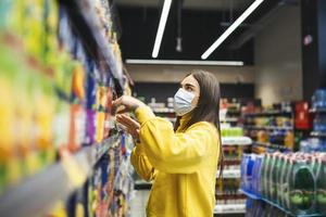 Woman wearing protective mask and buying food in grocery store during virus epidemic. young woman wearing a protective mask and gloves shopping in a time of virus pandemic, buying food supplies photo