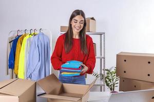 Young woman, owener of small business packing product in boxes, preparing it for delivery. Women packing package with her products that she selling online photo