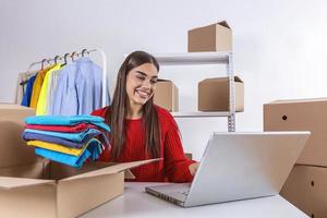 mujer empacando un artículo que vende en línea. mujer trabajadora en la tienda en línea. ella usa ropa informal y verifica la dirección de la computadora portátil del cliente y la información del paquete. pequeña empresa propietaria foto