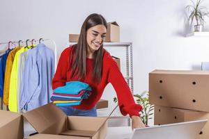 Woman packing item that she sells online. Working woman at online shop. She wearing casual clothing and checking on laptop address of customer and package information. small owner business