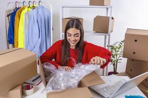 Working woman at online shop. She is wearing casual clothing and packaging goods for delivery. Owener of small business packing product in boxes, preparing it for delivery,checking on laptop address