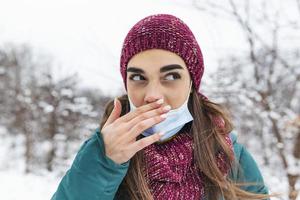 Young woman touching her nose with dirty hand. Avoid touching your nose. Woman wearing face mask rubbing her nose outdoor.Don't touch your face, stop spreading Coronavirus photo