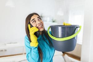 mujer sorprendida llamando a un plomero mientras recolectaba agua que se escapaba del techo usando un utensilio foto