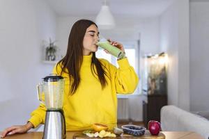 Woman drinking green detox smoothie drink. Happy smiling girl with glass of healthy fresh raw vegetable smoothie at home. Diet nutrition concept photo