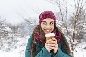 Happy young woman with disposable cup of coffee or tea wearing warm clothing. Beautiful girl holding disposable cup,standing outdoor on winter photo