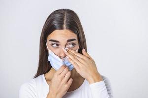 Don't Touch Your Face. Girl wearing surgical mask rubbing her eye with dirty hands.Precautions, Avoid Touching Your Eyes. Woman in medical mask rubbing her eye photo