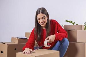 primer plano de una joven caja de cartón de embalaje. concepto de casa móvil. hermosa chica pegando una caja de cartón con cinta adhesiva. foto