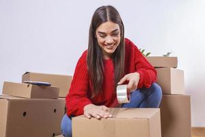 Close up of Young woman packing cardboard box. Moving house concept. Beautiful girl taping up a cardboard box with adhesive tape. photo