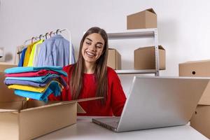 Woman packing item that she sells online. Working woman at online shop. She wearing casual clothing and checking on laptop address of customer and package information. small owner business photo