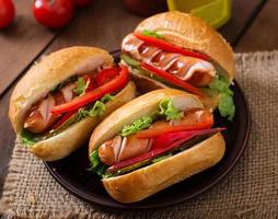 hot dog - sándwich con pepinillos, pimentón y lechuga sobre fondo de madera foto
