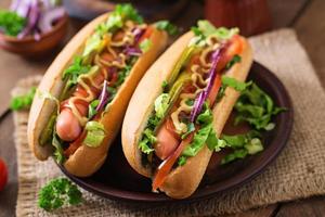 Hot dog with  pickles, tomato and lettuce on wooden background photo