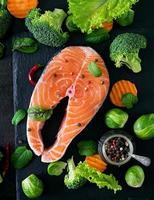 Raw salmon steak and ingredients for cooking on a dark background in a rustic style. Top view