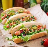 Hot dog with jalapeno peppers, tomato, cucumber and lettuce on wooden background photo