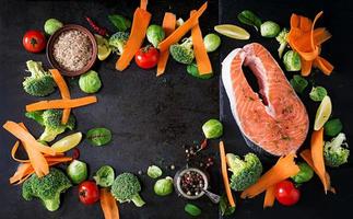 Raw salmon steak and ingredients for cooking on a dark background in a rustic style. Top view