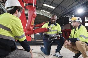 Male production engineers team discuss, test, and controls robotic arm in mechanical manufacturing factory, intelligent automatic machines in industrial business, and futuristic technology innovation. photo