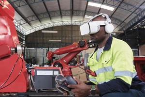 An African American engineer with VR glasses controls robotic arm, virtual simulator software in mechanical manufacturing factory, and intelligent automatic machines technology in industry innovation. photo