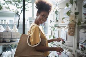 A Black female customer fills liquid soap into recycling jar from reusable containers in a zero-waste and refill store, smiles, and looks at camera, happy shopping in an environment-friendly shop. photo