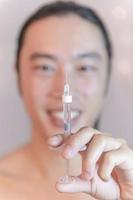 young Asian man holding injection with filler in front of his face. Asian man in beauty salon. plastic surgery clinic. photo