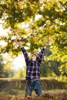 Adorable little boy plaing with yellow leaves in sunny autumn park photo