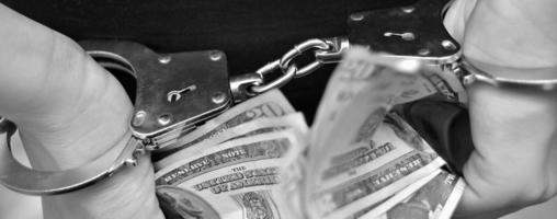 Man in handcuffs holding bribe money on dark background, closeup photo