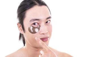 Beauty procedure and skin care. Close up portrait of relaxed topless man with beauty mask pads under his eyes. Isolated on white background. photo