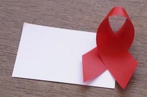 red ribbon and white empty paper on the wooden background, AIDS sign with copy space photo
