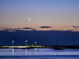 Moon crescent above a seaside pier in the morning photo