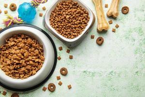 A bowl with dog food, dog treats and toys on a wooden floor. photo