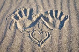 huella de mano con corazón en la arena de la playa. arena ondulada naturaleza muerta en la orilla del mar foto