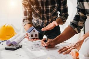 Close up shot of scale model house on table with architects. Two architects making architectural model in office together. photo